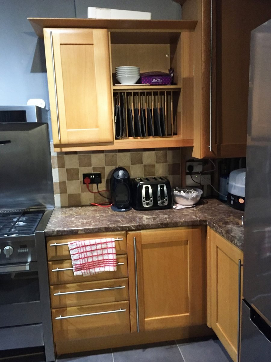 A dated kitchen with orange-toned units and a red tiled splashback