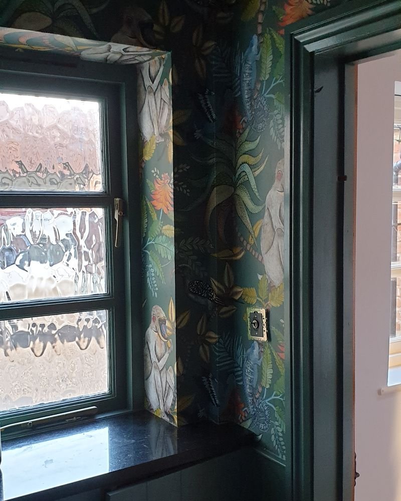 A cloakroom in bold botanical wallpaper above dark green panelling