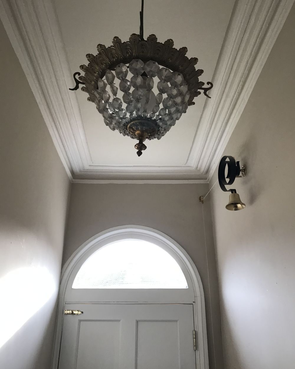 A restored period hallway with ornate cornice, arched fanlight door and original chandelier