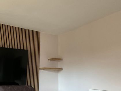A living room painted in soft white beside a slatted wood feature wall