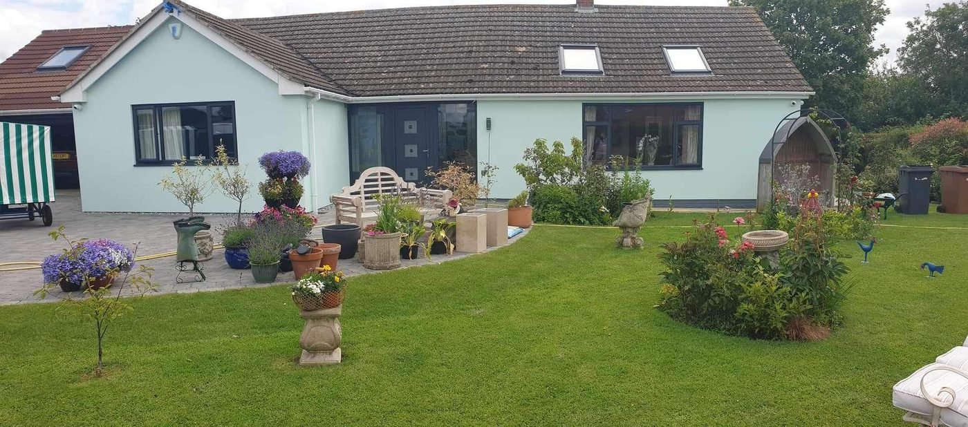 The finished bungalow in pale mint render, seen across the garden