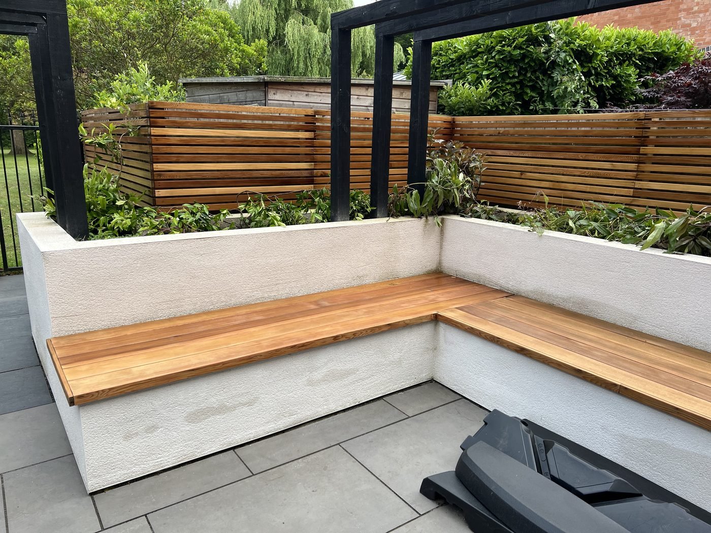 The finished rendered bench with a hardwood seat under the black-framed pergola