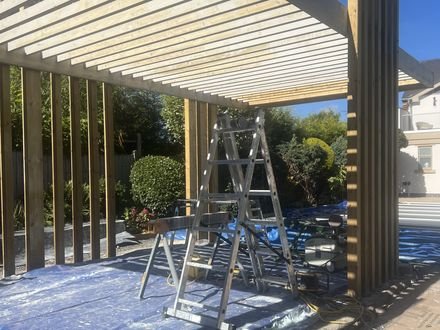 A slatted timber pergola going up, the ground sheeted