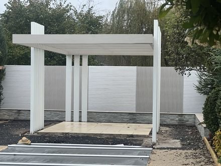 A pergola painted white in front of a white slatted fence