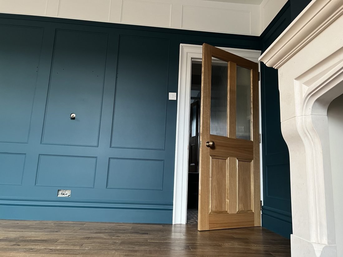 A reception room in deep teal panelling with an oak door and stone fireplace