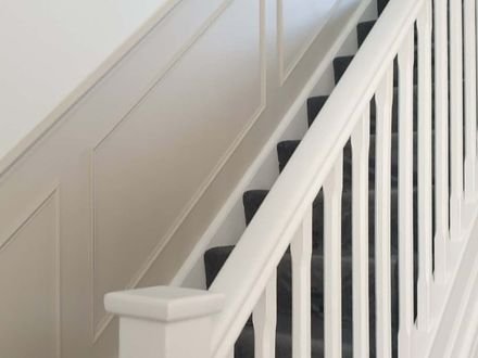 White box-moulding panelling carried up a staircase beside a painted balustrade