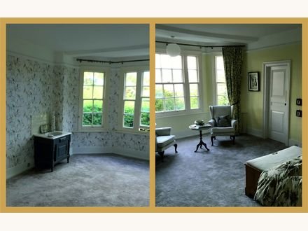 A bay-window bedroom papered in a trailing botanical print, seen from two sides