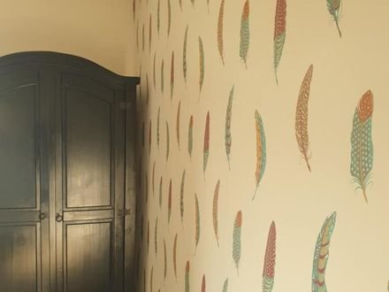 Feather-pattern wallpaper beside a dark painted wardrobe