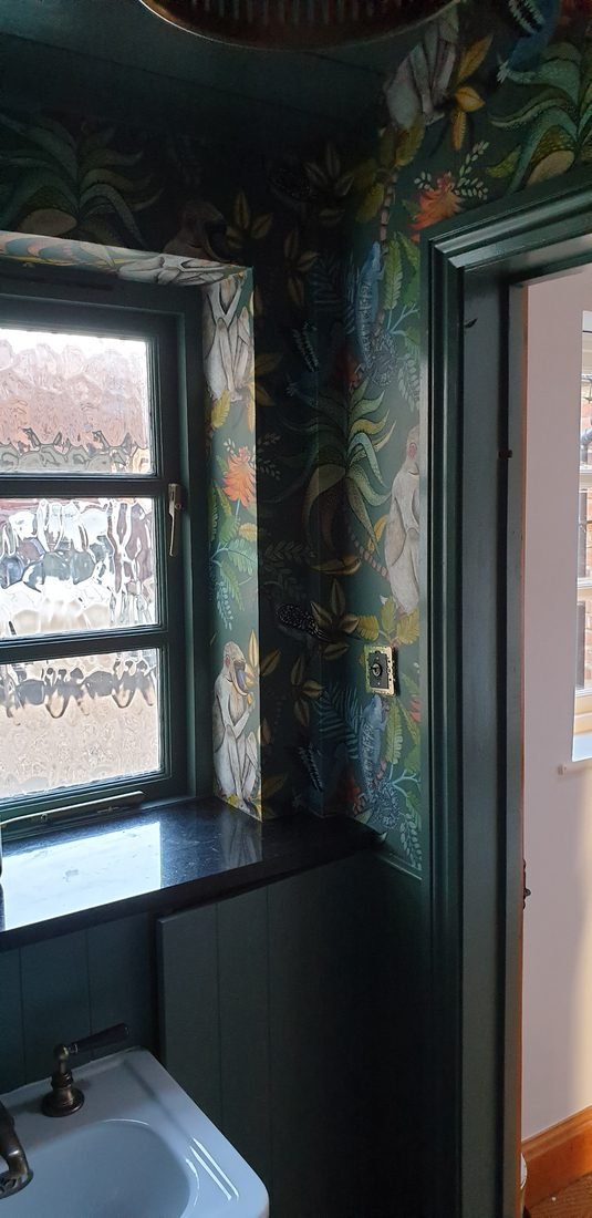 A cloakroom in bold botanical wallpaper above dark green panelling